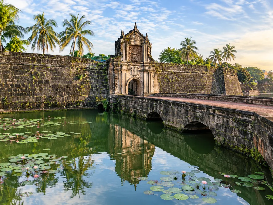 Ang berdeng moat sa ibaba ng mga pader ng Fort Santiago, may mga dahon ng water lily at batong tulay papunta sa tarangkahan